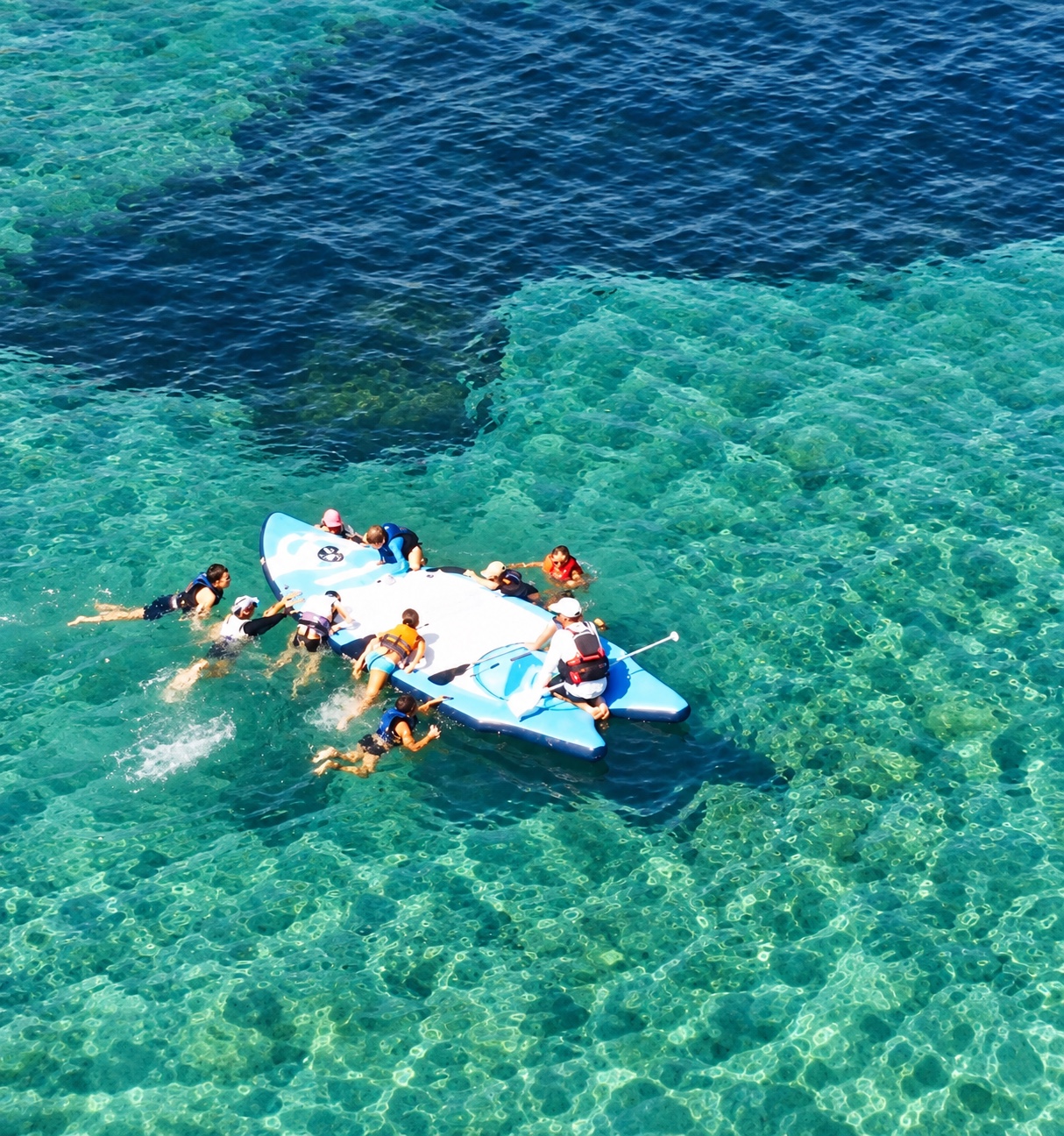 Un groupe partage un moment de baignade autour d’un paddle géant sur une eau turquoise.